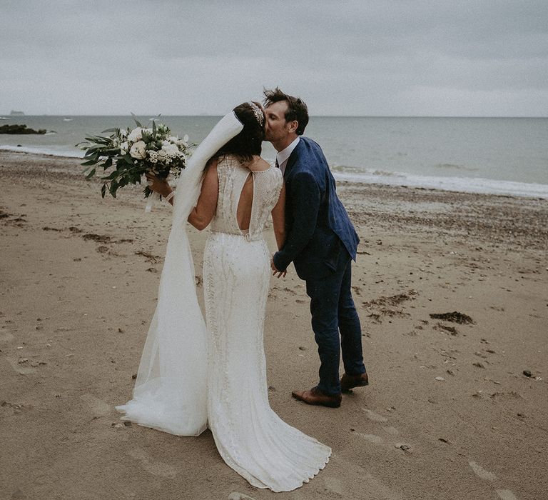 Bride & groom kiss on the beach after wedding ceremony