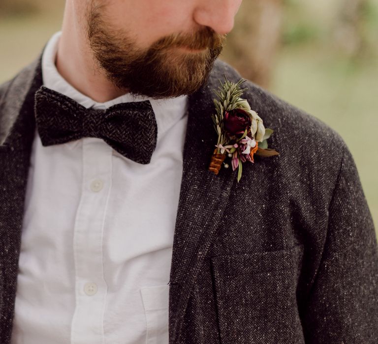 Groom in grey tweed suit jacket, white shirt and tweed bow tie with red rose buttonhole