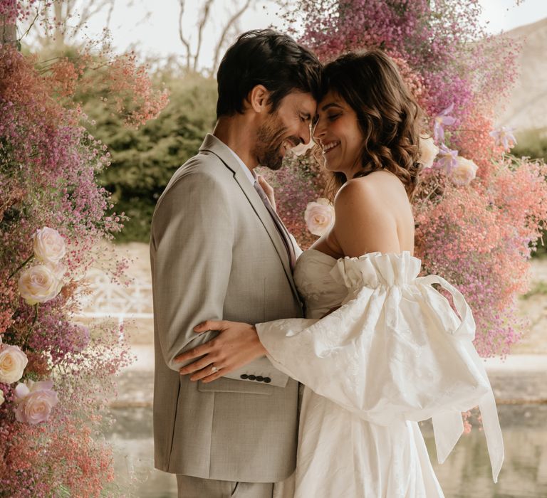 Bride & groom touch heads as pastel florals can be seen in the background