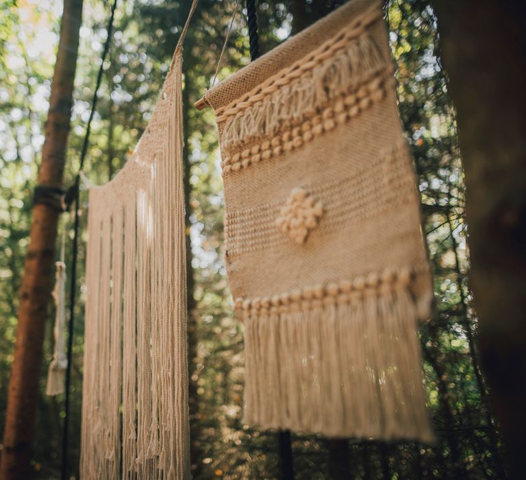 Macrame decor hangs in trees at woodland wedding