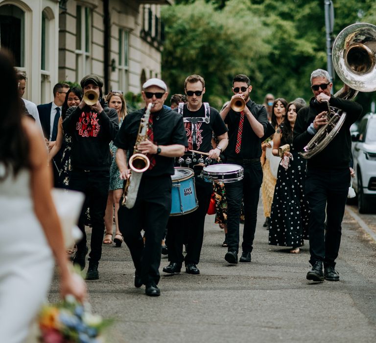 Bride in white strapless Rebecca Vallance Dress walks through streets of Harrogate followed by the New York Brass Band and wedding guests