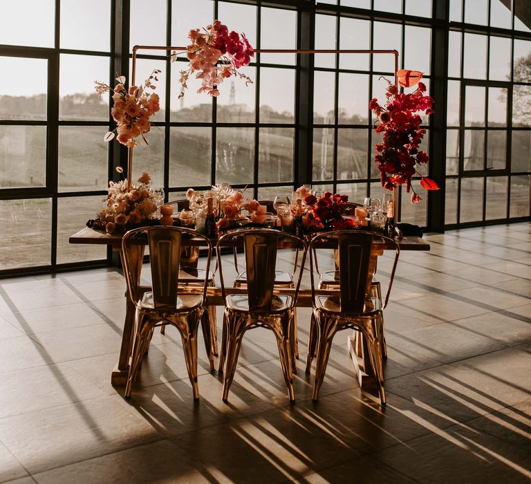 Industrial wedding venue tablescape with flower installation, metal chairs and red flowers