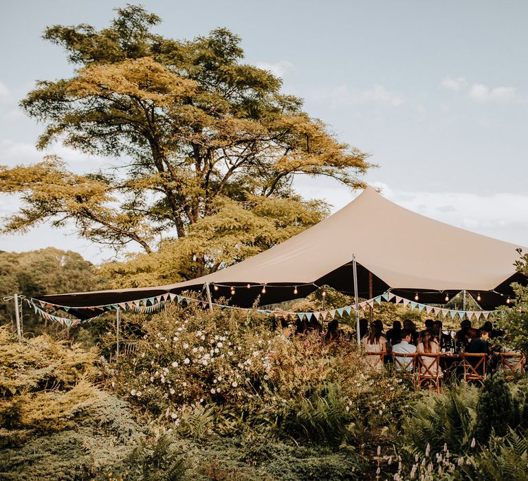 Exterior of grey tipi with string fairy lights and bunting at garden wedding reception