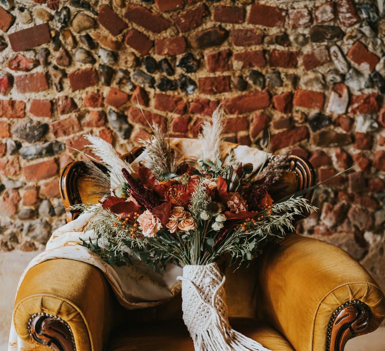 Vintage mustard velvet armchair with large bouquet of red and peach roses, carnations, thistles, wild grasses and foliage 