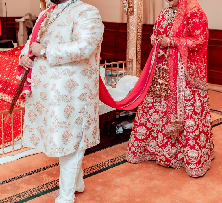 Bride walks whilst holding grooms sash around the room during Sikh wedding