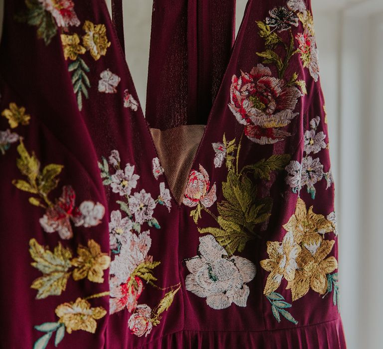 Colourful floral embroidered burgundy bridesmaids dress hangs up before barn wedding ceremony