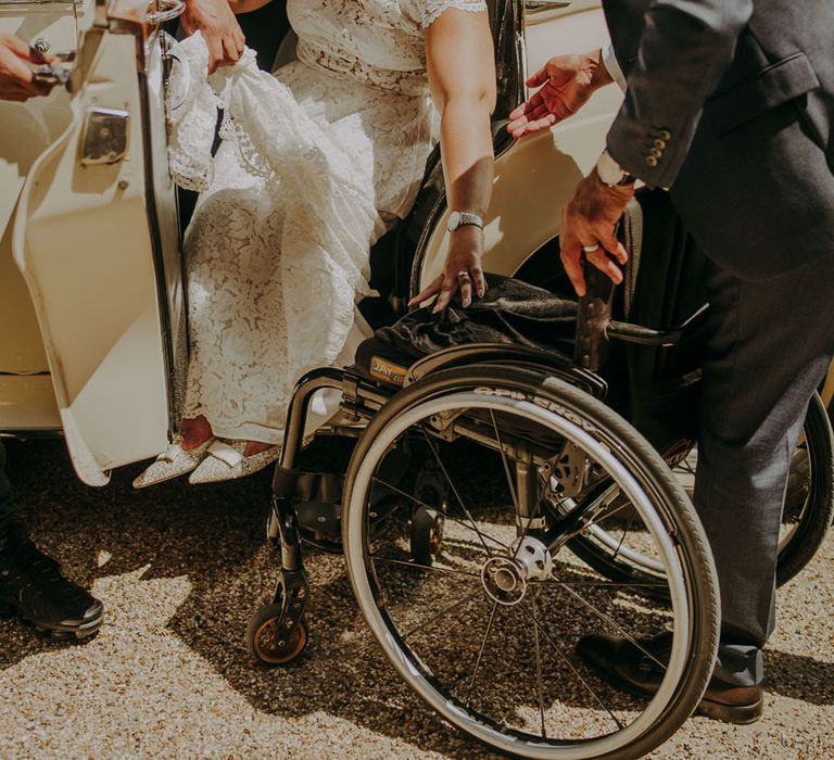 Bride in a lace wedding dress and embellished shoes getting out of her vintage wedding car into her wheelchair 