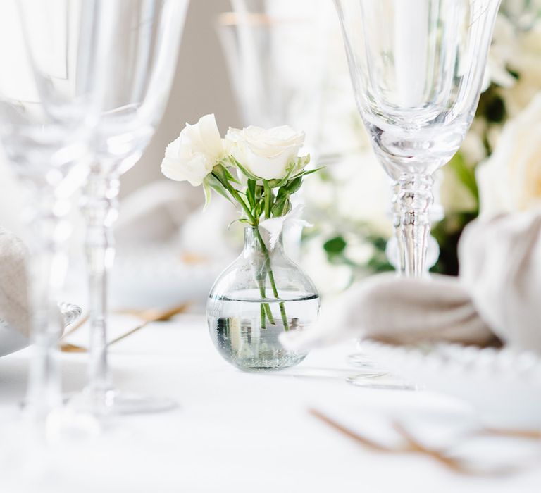 A bud vase filled with lithianthus sits between gold rimmed glassware. 