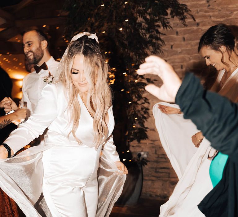 Blonde bride dances during reception whilst wearing bridal jumpsuit and veil