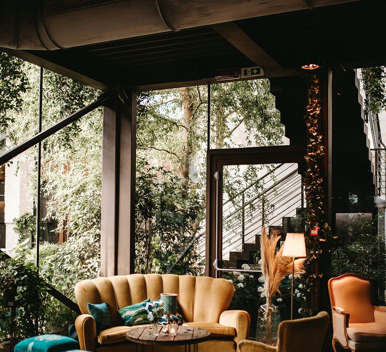 Boho chic seating area with orange velvet sofa and chairs and emerald green cushions 