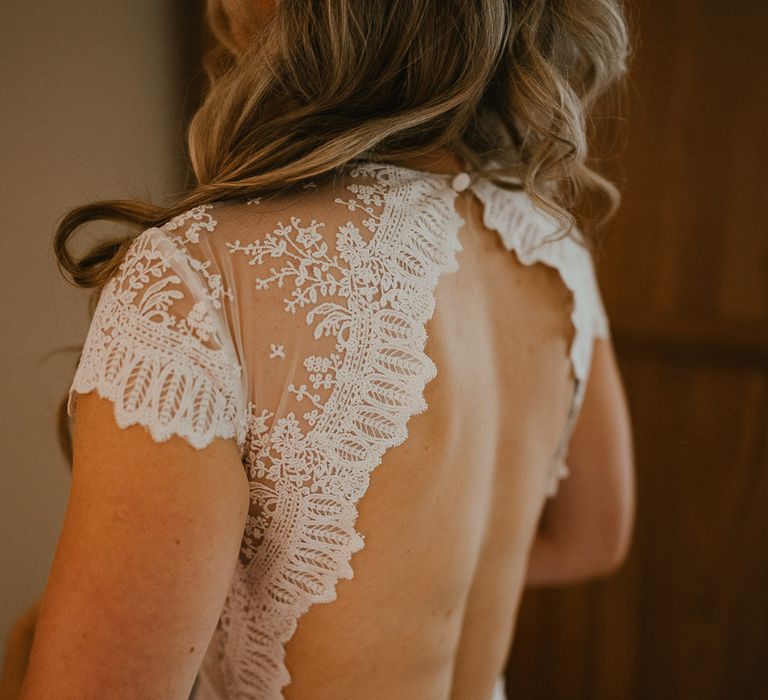 Bride with curled blonde wedding hair wears open back lace cap sleeved wedding dress before late summer wedding in Norfolk