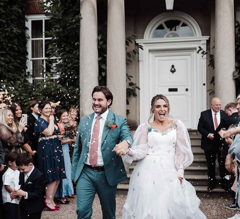 Confetti moment at Iscoyd Park wedding venue with groom in a blue suit and bride in an embroidered Victoria Sanders bespoke wedding dress 