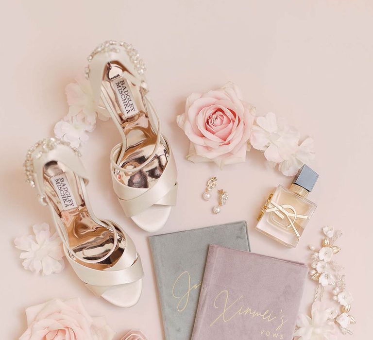 Pale satin wedding shoes beside wedding jewellery and velvet stationery book containing vows