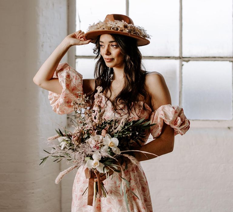 Boho bride in patterned bridal separates and a fedora hat decorated with dried flowers 