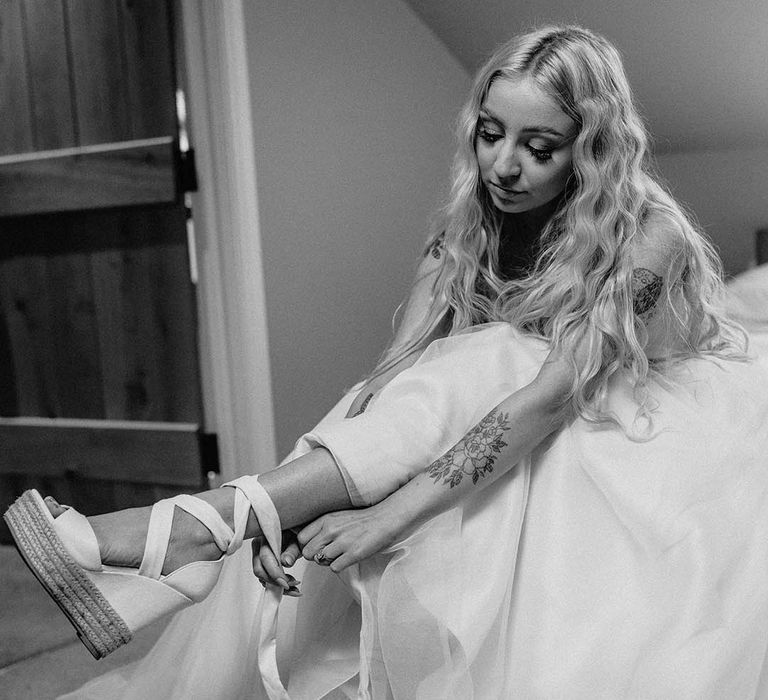 Bride ties up her wedge wedding shoes