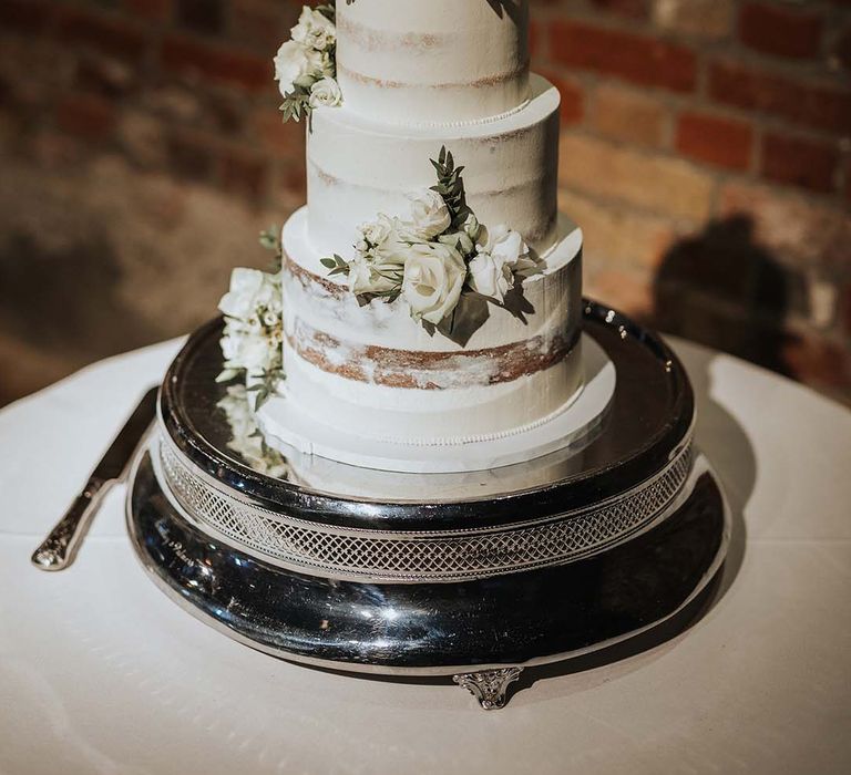 Three-tier semi-naked wedding cake with white frosting and white rose decoration