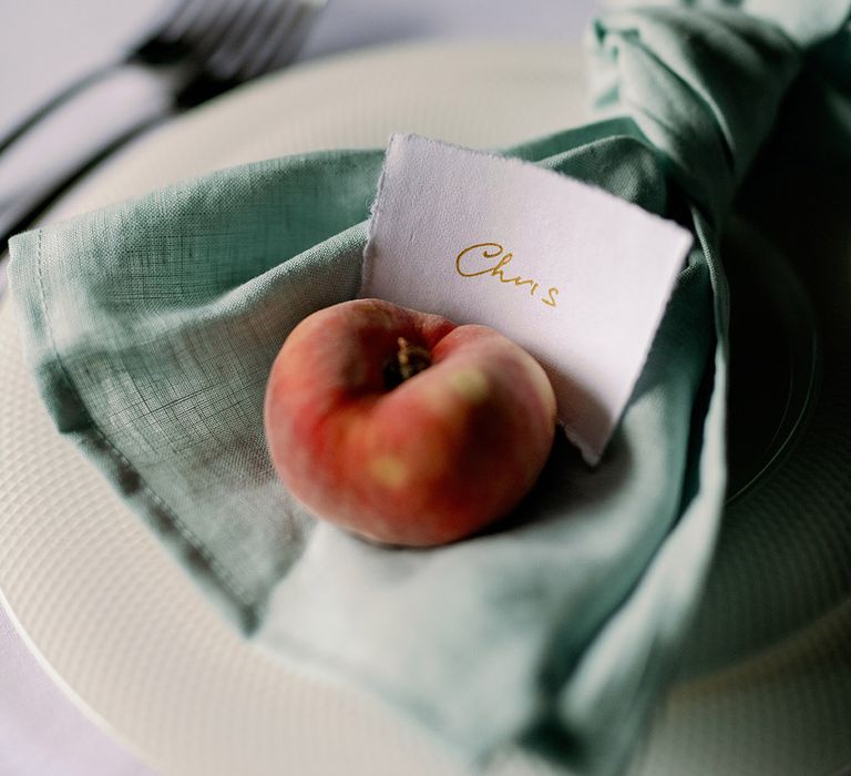 Green napkin with handwritten name place cards and a single peach for table setting