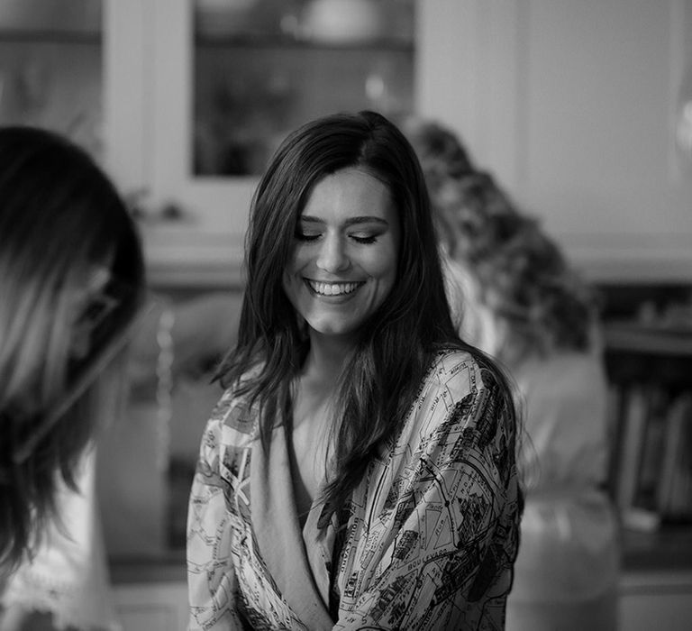 Bride in map patterned satin robe smiling as she gets ready for her wedding day