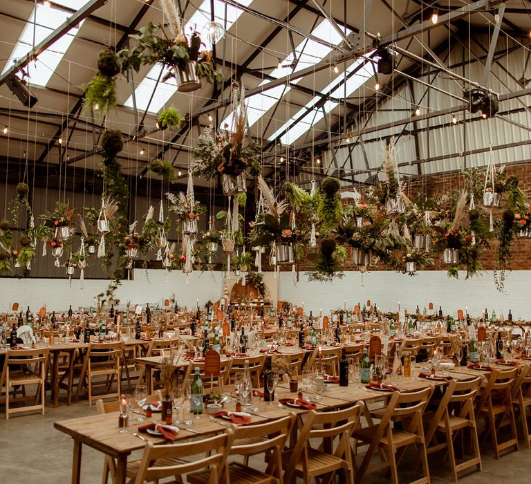 Industrial warehouse wedding venue complete with DIY hanging plant decor and flower cloud with orange accents 