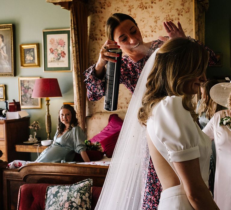 Bride in puff sleeve cutout back wedding dress gets her hair styled for the wedding day with wedding guests looking on