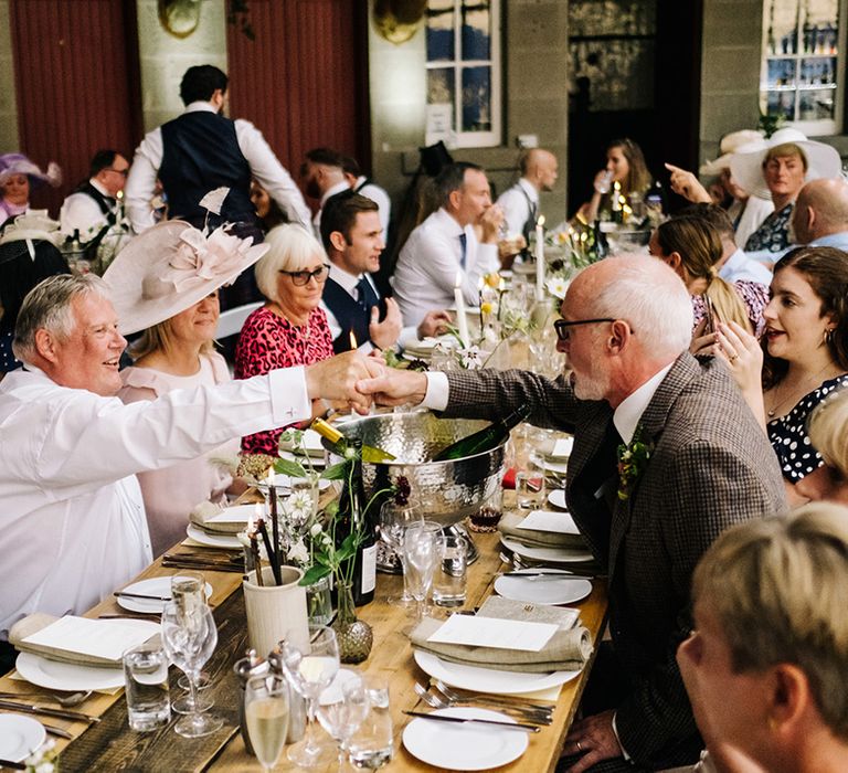 Guests shake hands over long wooden banquet style tables for wedding reception at Errol Park 