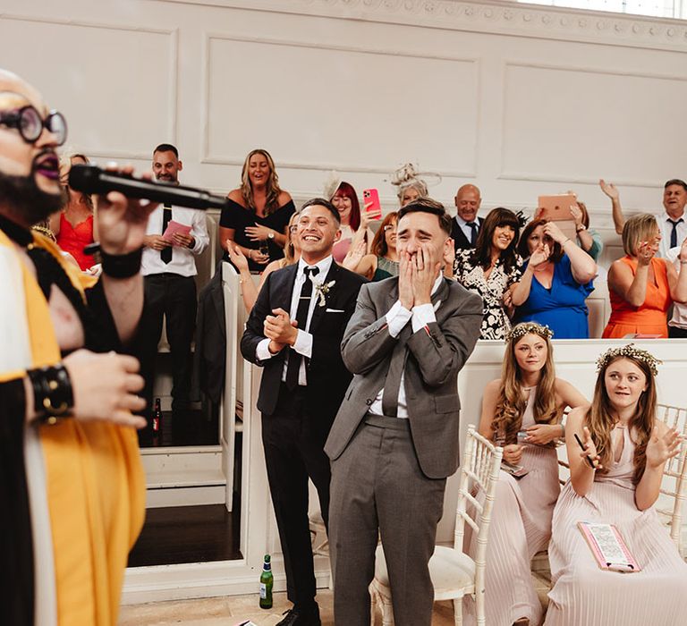 Wedding guests enjoy the drag entertainment as the grooms laugh together 