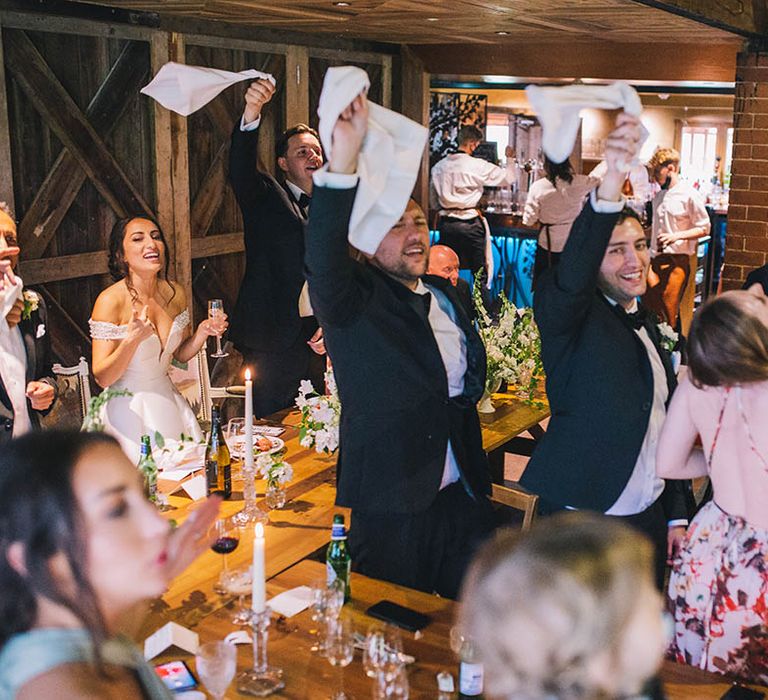 Wedding guests and bride and groom stand and wave their napkins in celebration