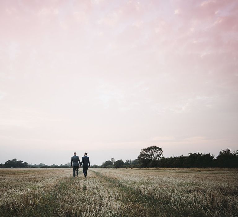 Grooms walk hand in hand in a field 