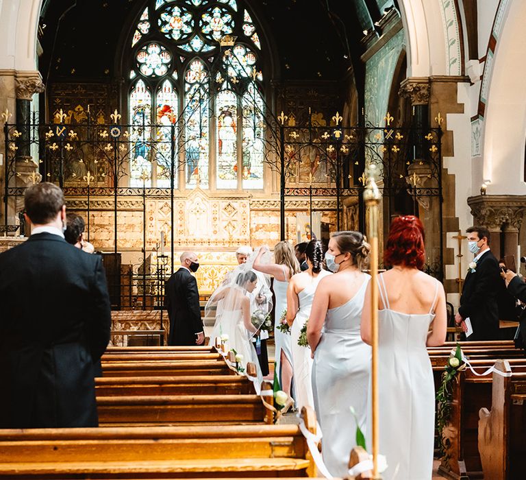 Bride pulls her veil away from her face as the bridesmaids continue walking down the aisle 