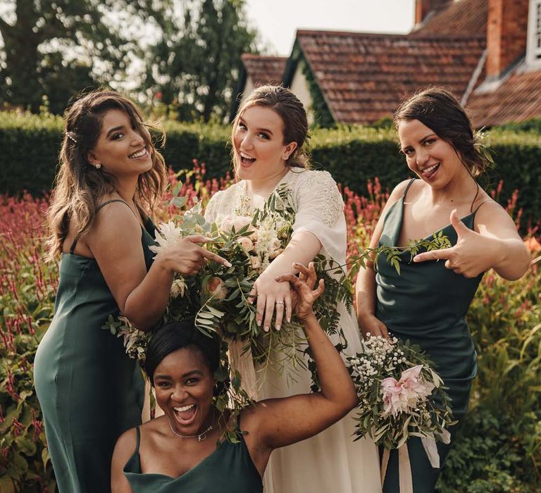 Bridesmaids in satin green cowl neck bridesmaid dresses point to the bride's engagement ring in lace wedding dress 