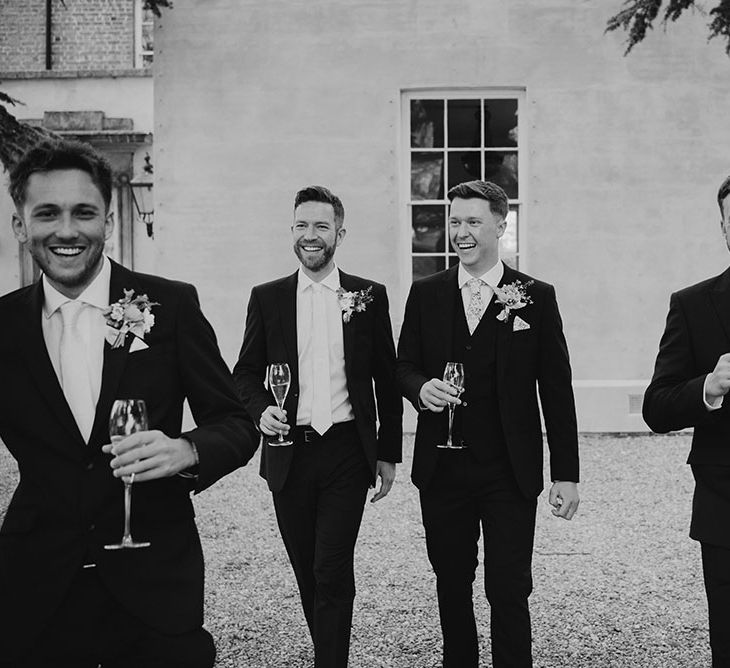 Groom walks with his groomsmen outdoors wearing suits at Aswarby Rectory 