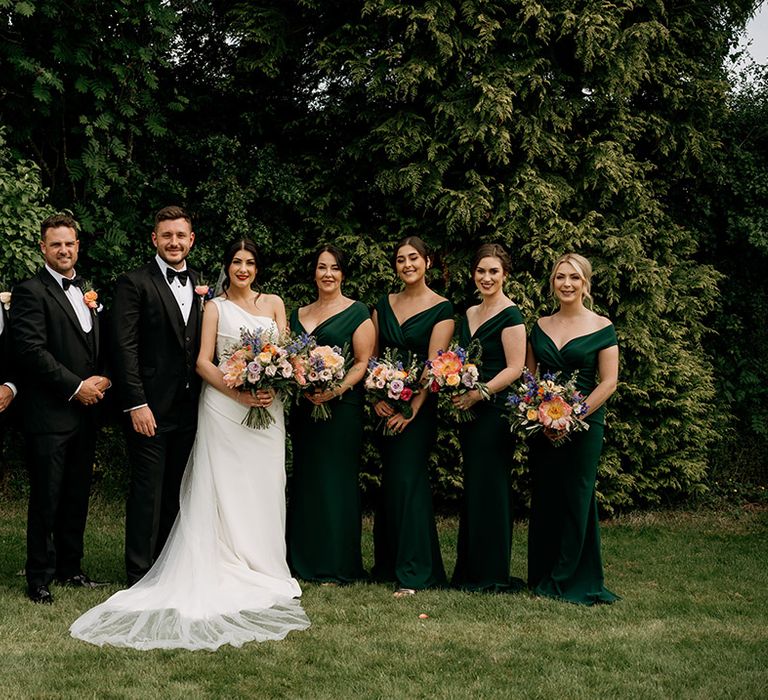 Bride and groom with the wedding party with the bridesmaids in green dresses and groomsmen in black tie 