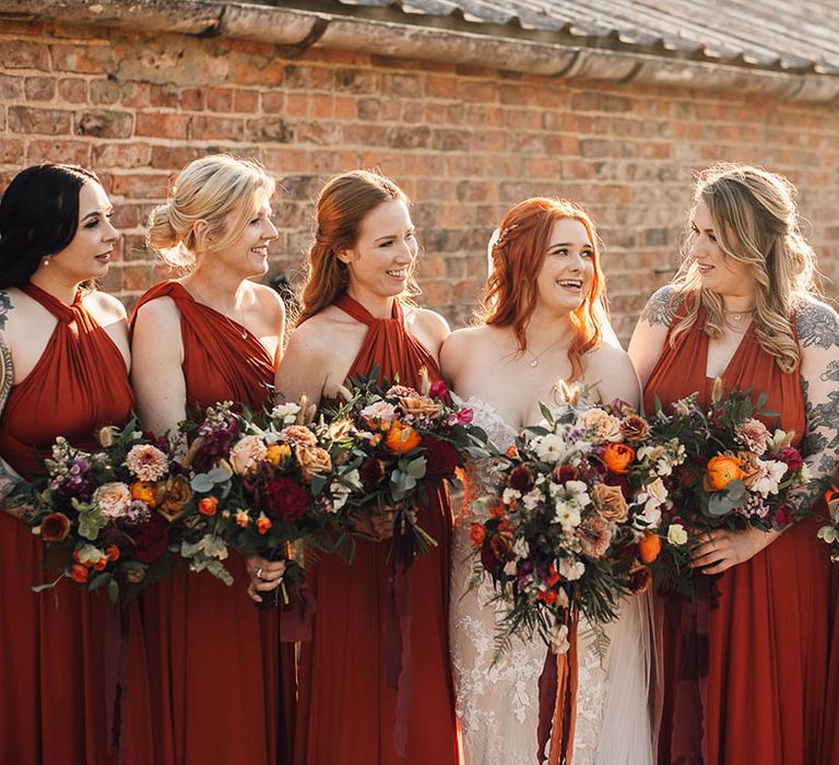 Bride in fitted boho wedding dress with bridesmaids in orange dresses with autumnal bouquets