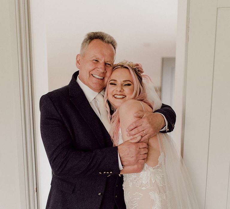 Bride with pink hair and wearing Jane Hill lace fitted gown hugs her father on the morning of her wedding day