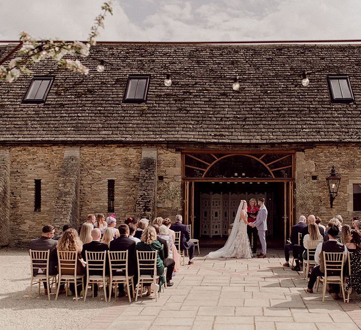 Bride & groom marry Oxleaze Barn in outdoor wedding ceremony as festoon lighting hangs above them 