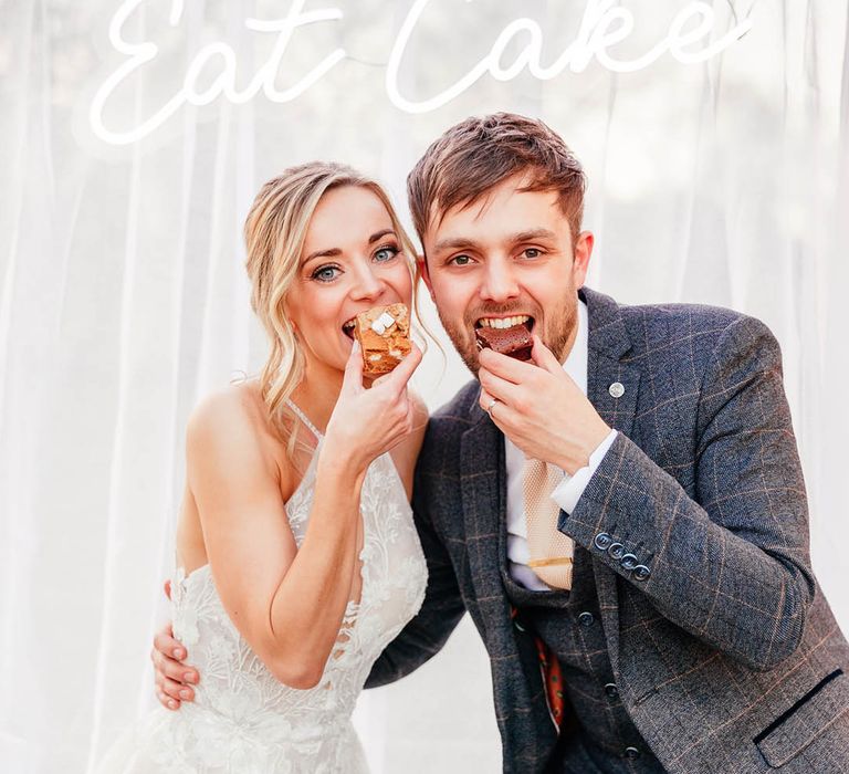 Bride and groom eat some sweet treats in front of a white neon sign 