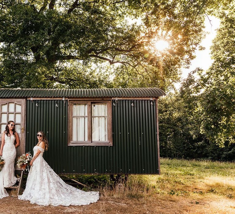 Brides pose next to caravan together wearing sunglasses 