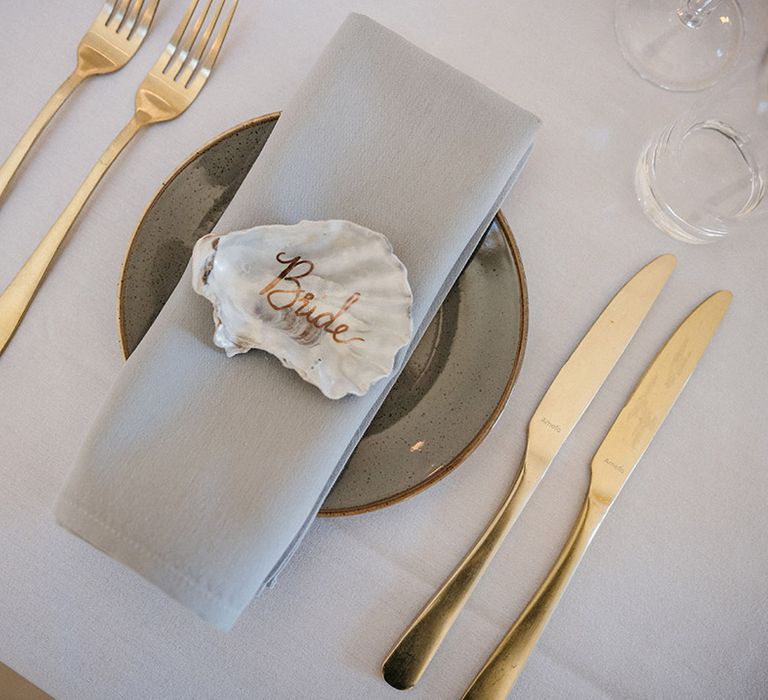 Gold cutlery with a shell name place setting with grey napkin