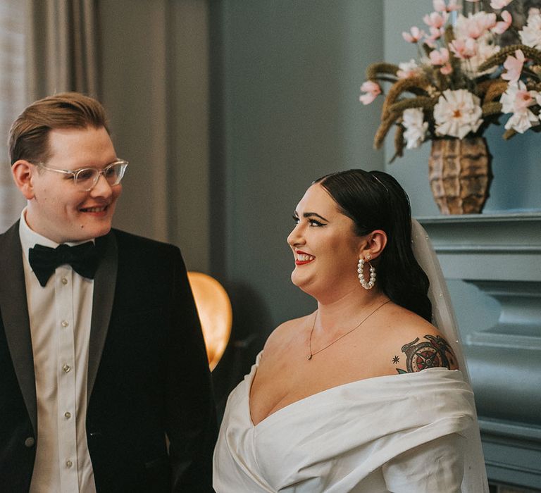 Groom wears black tie and glasses as he looks lovingly at his bride during Old Marylebone Town Hall wedding ceremony