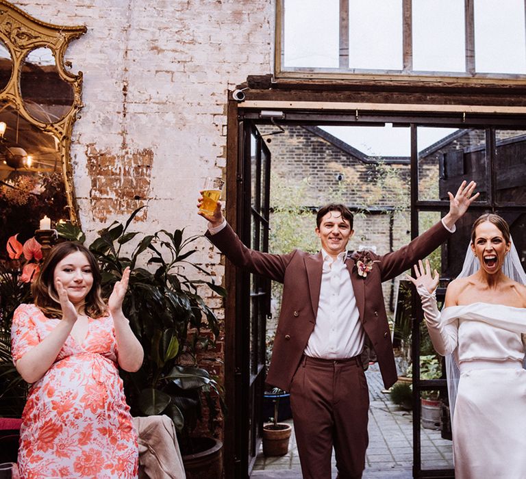 Bride in an off the shoulder long sleeve wedding dress enters the reception with the groom holding a pint