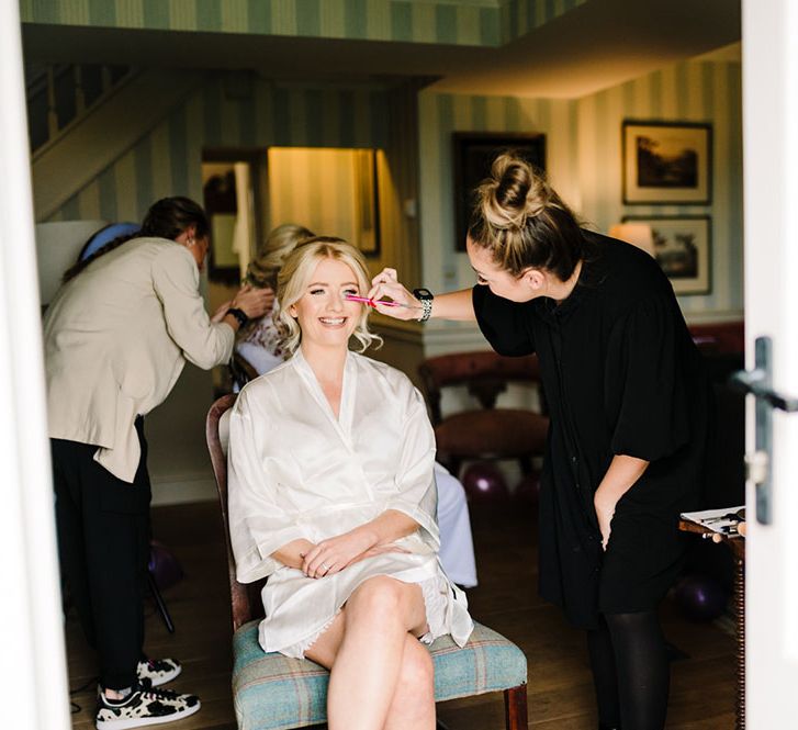 Blonde bride wears silk dressing gown on the morning of her wedding day whilst having her makeup done 