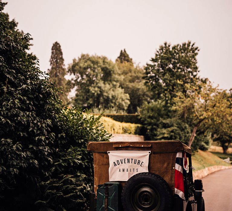 Black Jeep wedding car transport with a white sign reading 'Adventure Awaits' 