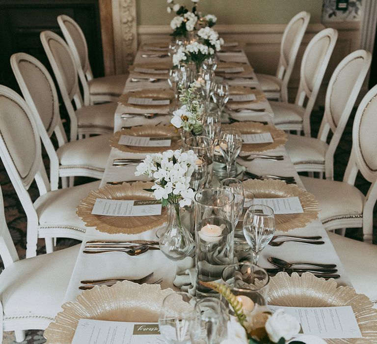 White and sage green wedding tablescape with gold details with green runners and gold chargers