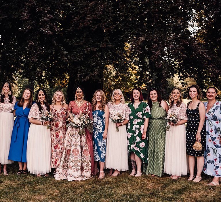 Bride stands with wedding guests in colourful outfits outdoors 