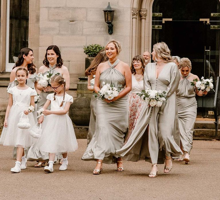 Bridesmaids wear sage green bridesmaid dresses in differing styles and hold white classic floral bouquets 