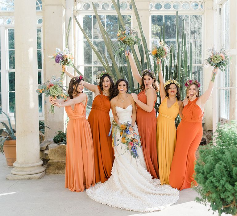 Bride in Emma Beaumont design wedding dress stands with her bridesmaids in ombre styled orange and yellow bridesmaid dresses 