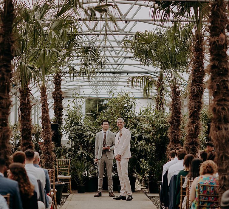 Groom waits at the bottom of the palm tree lined aisle for Bride