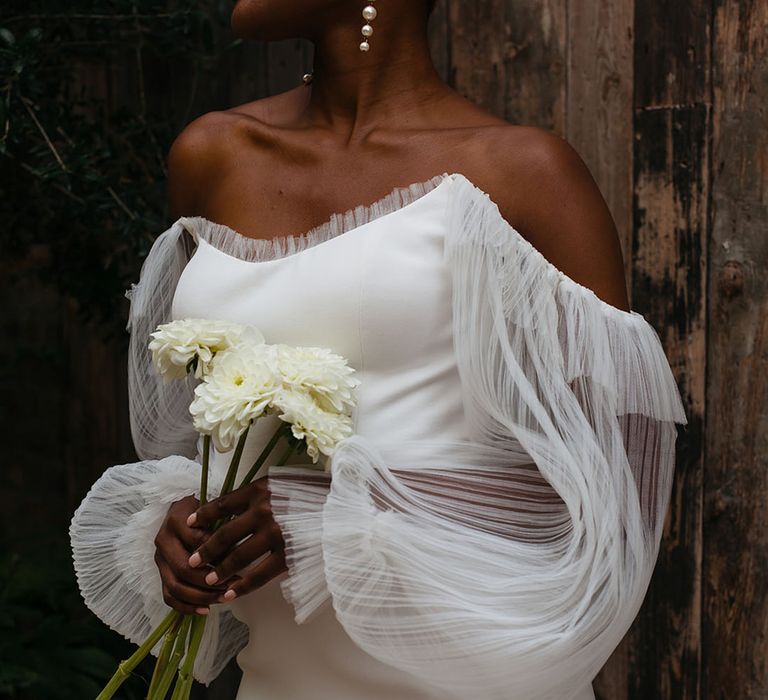 Bride wearing pearl drop earrings and long lace sleeves holding bunch of white dahlias laughing at 100 Barrington wedding with black and white table decorations