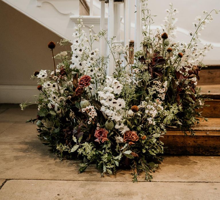 Dark red and white wedding flower arrangement sitting at the bottom of the stairs 