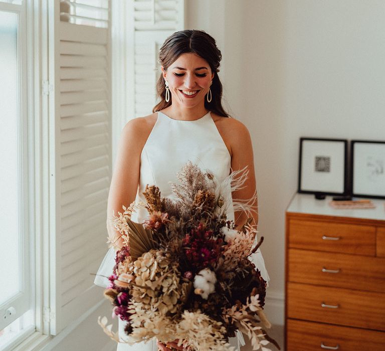 Bride in high neck wedding dress holding dried flower bouquet with palm leaves and grass